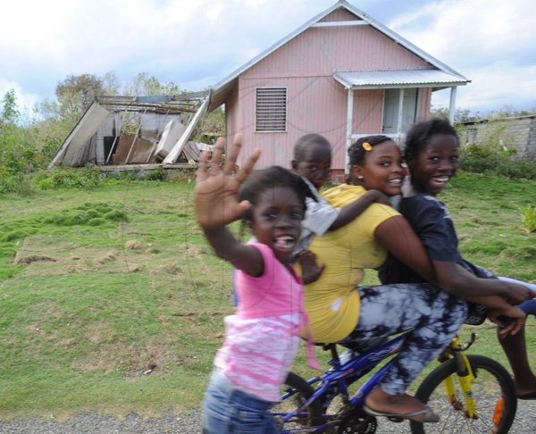 Ricardo Makyn/Staff Photographer 
Children wave to the Gleaner Photographer while riding by a House that section of it was blown down in Sandshore   Manchioneal Portland  due to  the passage of Hurricane Sandy