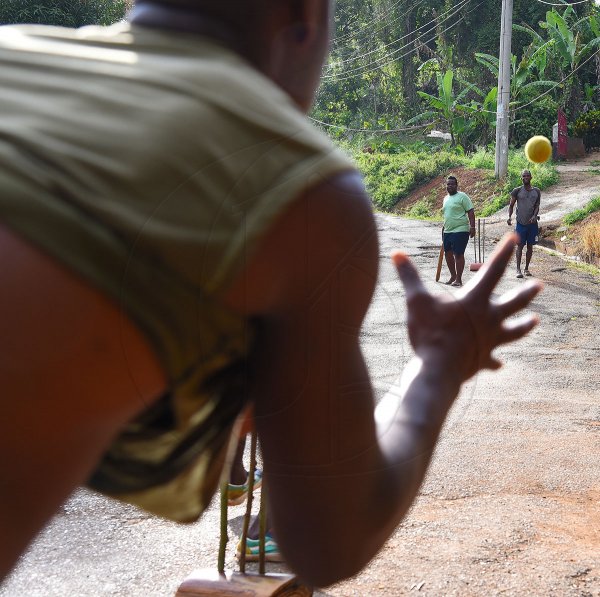 A bowler catches the ball as young men at Junction crossroads in St Catherine play ricket in the streets on Tuesday to take their minds of the COVID-19 outbreak. Twenty-six people have tested positive for the virus and one man has died.