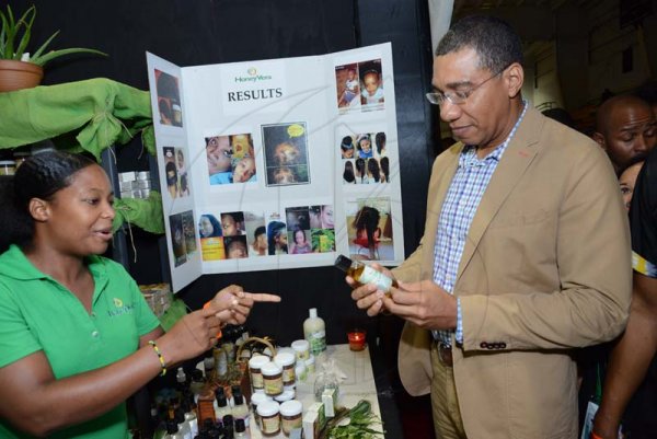 Rudolph Brown/ PhotographerChristal-Ann Thompson, Founder and CEO of Honey Vera, give the Prime Minister Andrew Holness one of her Hemp product during a tour of the JEA JMA Expo Jamaica at the National Indoor Sports Centre and the National Arena on Sunday April 22, 2018