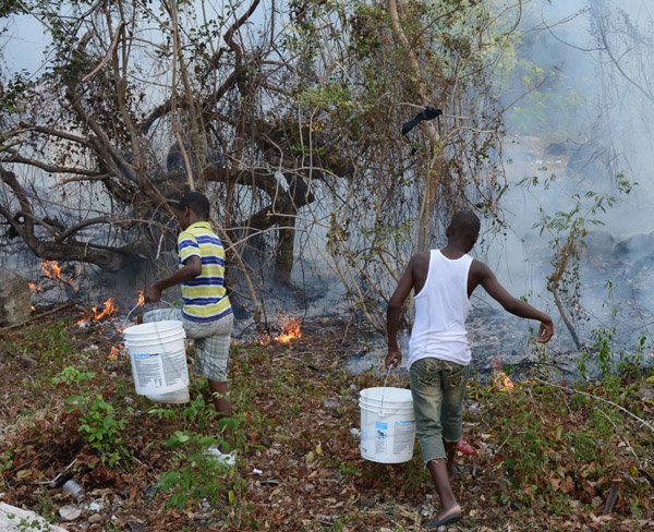 Ian Allen/Photographer
Residents stand ready with buckets of water to put out a bush fire if it gets too close to their house which has been raging in Western St Thomas for over a week, threathens this house in Gordon Castle, Llandewey St Thomas. The fire, which is believed to be caused by the unwise slash and burn practice, has caused massive devastation in the surrounding areas of Richmond  Gap, Orange Tree  and Albion Mountain. Thousands of fruit trees such as mangoes and ackees have been destroyed. Several goats have perished in the blaze.