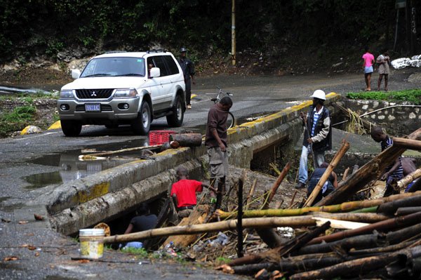 Ricardo Makyn/Staff Photographer
A motor vehicle passes residents feverishly trying to remove debris from the Flat Bridge in the Bog Walk Gorge in St Catherine on Monday 27.8.2012. There was limited access to the gorge yesterday morning.