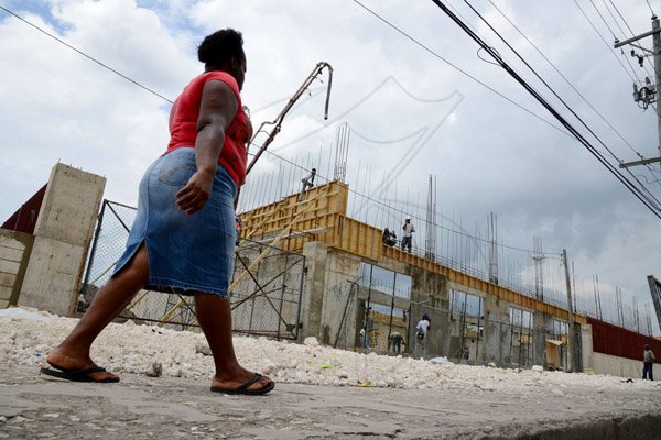 Ricardo Makyn/Staff Photographer 
A lady walks by a building under construction on Burke Road in Spanish Town.