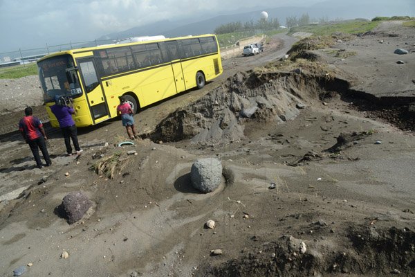 Rudolph Brown/PhotographerA JUTC bus pass has workmen's remove a pile up of sand and silt from the palisadoes main road in Kingston from High tides and high winds, related to Hurricane Matthew on Saturday, October 1, 2016