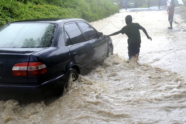 Norman Grindley/Chief Photographer
A young man guides a motorist through flood waters at the Eleven Miles, Bull Bay ford in St. Andrew during heavy rains on Sunday.