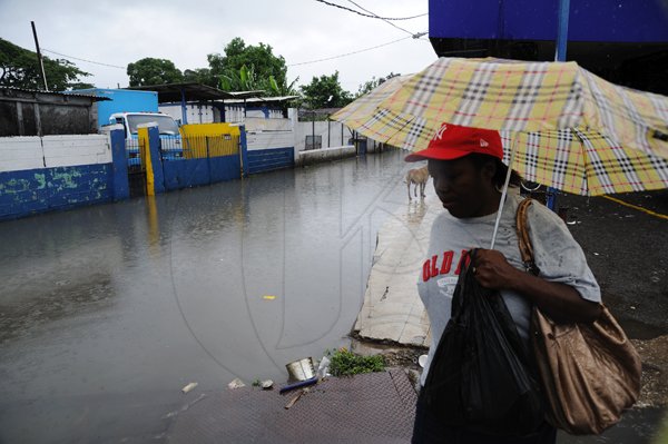 Ricardo Makyn/Staff Photographer
A Woman walks by  flooded street that runs of Burke road adjacent to the Bus Terminal in Spanish Town St Catherine due to the continued Rains of the last week on Sunday 5.6.2011
