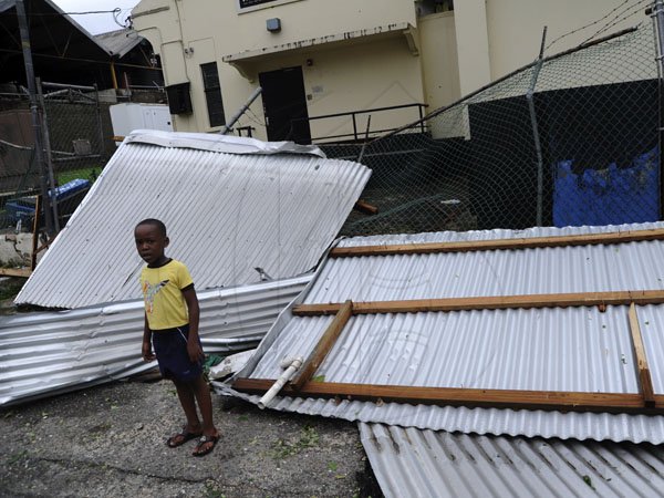 Ricardo Makyn/Staff Photographer
A a child stands next   sheets of ZINC in the  Stony Hill square  St Andrew