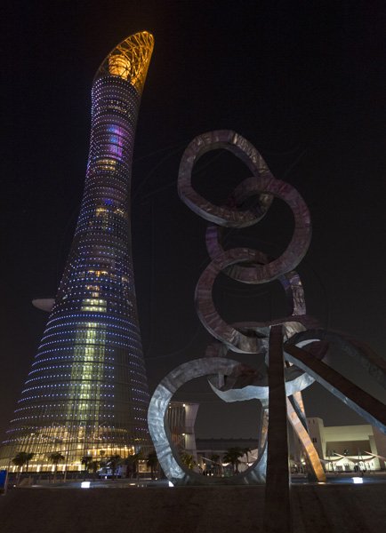 The illuminated Torch Tower Doha (left) also known as the Aspire Tower and Khalifa International Stadium olympic ring sculpture at night. The Tower houses a five-star hotel, a sports museum among other amenities. The hotel is located in the Aspire Zone Complex in close proximity of the Khalifa International Stadium in Doha, Qatar.