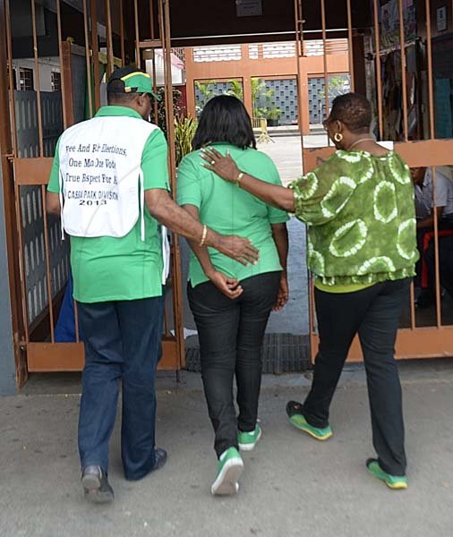 Ian Allen/Staff Photographer
Edmond Bartlet left and Olivia Grange right, escorts Beverly Prince centre into the Polling Station at the  Half Way Tree Primary School in St.Andrew to vote during the Cassia Park Division Bi-Election on Thursday.