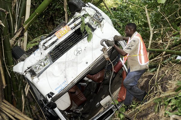 Ian Allen/Photographer
A recovery worker places a hook on a Coaster bus so it can be pulled out of a ravine in Brandon Hill, St.Andrew.