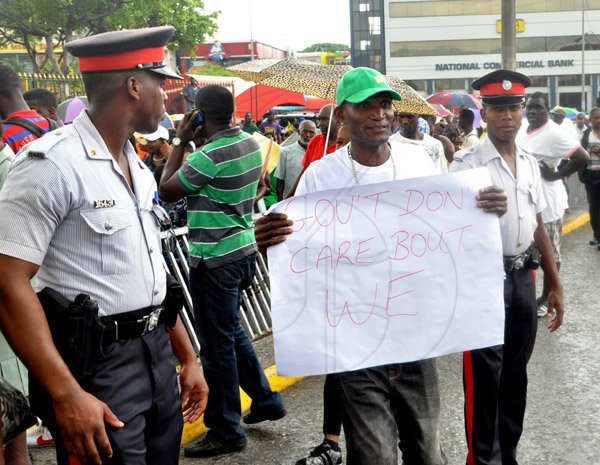 Jermaine Barnaby/Photographer
Police watches as a protestor walks by with placard in hand as he and scores of others protested against bus fare increase in Half way Tree on Monday August 25, 2014.