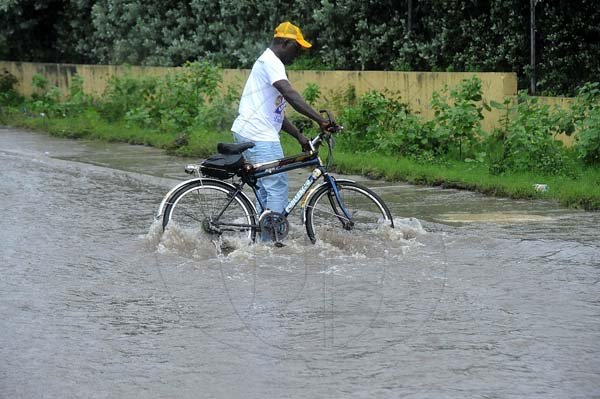 Ian Allen/Photographer
A pedal cyclist tries to cross gushing water along Spanish Town road in the vicinity of Delacree Park Housing scheme as heavy rains pelt the Island on wednesday.