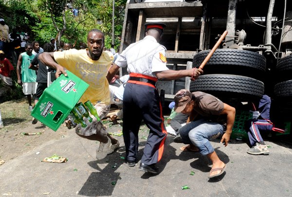 Ricardo Makyn/Staff Photographer.
A policeman uses his baton in attempts to disperse looters on the scene of an accident in which a truck transporting Heineken beer along the Linstead Bypass in St Catherine.The accident also involved a Toyota motorcar, the driver of which was killed. The truck driver was badly burnt as the truck caught fire before residents went on a looting spree.
