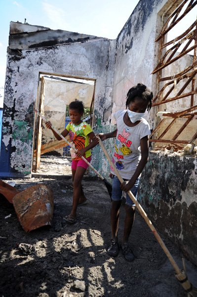 Norman Grindley /Chief Photographer
Seven-year-old Mickailla March, (left) and Shadeka Hanson, 10 both members of Hannah in Town police youth club in West Kingston, put in some labour day work on their burnt out police station yesterday. Residents turned out and clean debris from the station, as they call on the authority to rebuild the station.