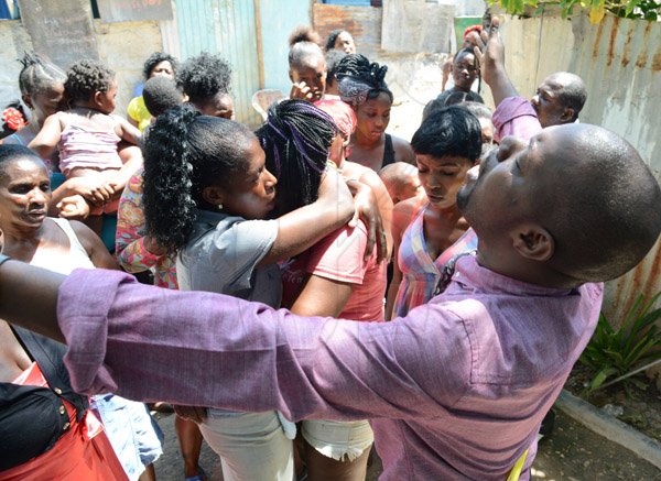 Rudolph Brown/PhotographerElder Omar Ricketts praying for Sonia McDonald, (centre) mother of two of the person that kill and members of the family after gunmen shoot up seven killing five including three children and set their home ablaze at Africa settlement in March Pen Community in Spanish Town on Sunday, October 9