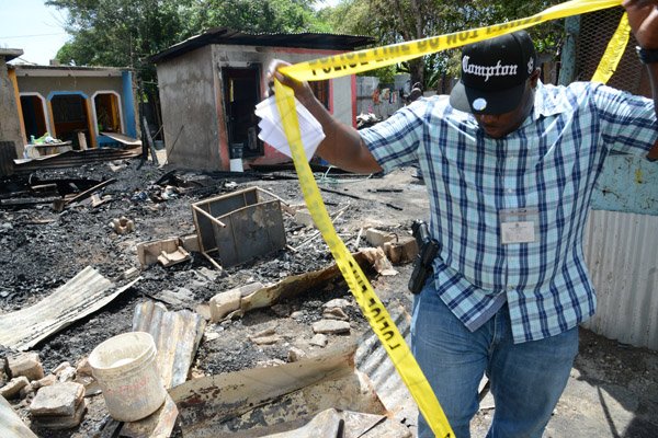 Rudolph Brown/PhotographerA police officer secure the crime scene after gunmen shoot up seven killing five including three children and set their home ablaze at Africa settlement in March Pen Community in Spanish Town on Sunday, October 9