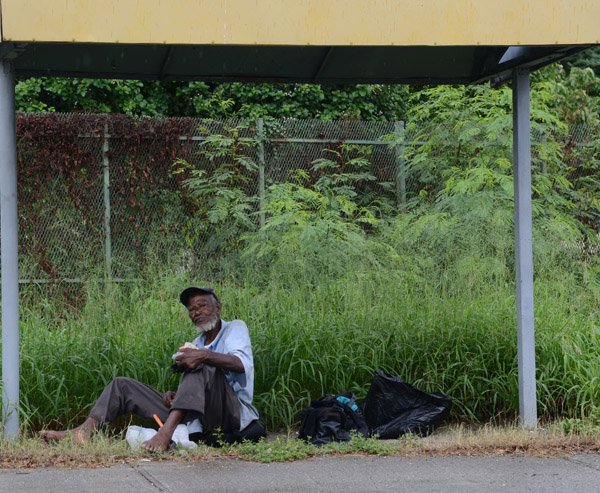 Gladstone Taylor/ PhotographerA homeless man is seen having an afternoon meal while sheltering from the rain beneath a bus stop on  Arthur Wint Drive on monday october 3, 2016