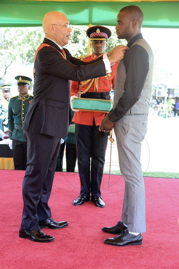 Lionel Rookwood/PhotographerTremayne Sheldon Oshawn Brown recieves The Batch Of Honour For Gallantry for his act of bravey displayed when he jumped into a gully with gushing rainwater to save the life of 12 year old Renaldo Reynolds in Trench Town from Governor General Sir Patrick Allen at The National Awards held at King's House on Monday October16,2017. *** Local Caption *** Lionel Rookwood/PhotographerA picture of humility is Tremayne Sheldon Oshawn Brown as he receives The Badge Of Honour For Gallantry for his act of bravey displayed when he jumped into a gully with gushing rainwater to save the life of 12-year-old Renaldo Reynolds in Trench Town. He is no swimmer but he didn't even think of that. Here he receives his award from Governor General Sir Patrick Allen at The National Awards held at King's House, yesterday.