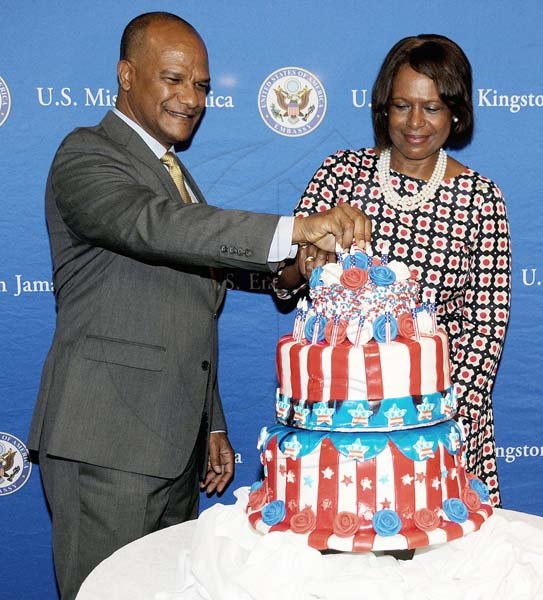 Winston Sill/Freelance Photographer
United States Ambassador Pamela Bridgewater joins hands with Security Minister Peter Bunting in cutting the red, white and blue Independence day cake  in honour of the 4th of July celebrations last Thursday.
